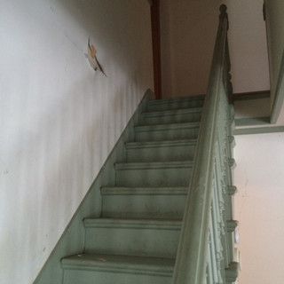 A set of stairs with a wooden railing and a white wall.