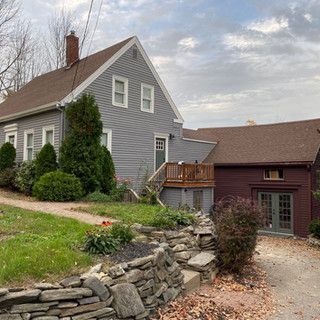 A large gray house with a stone wall in front of it.