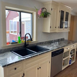 A kitchen with a sink , dishwasher , cabinets and a window.