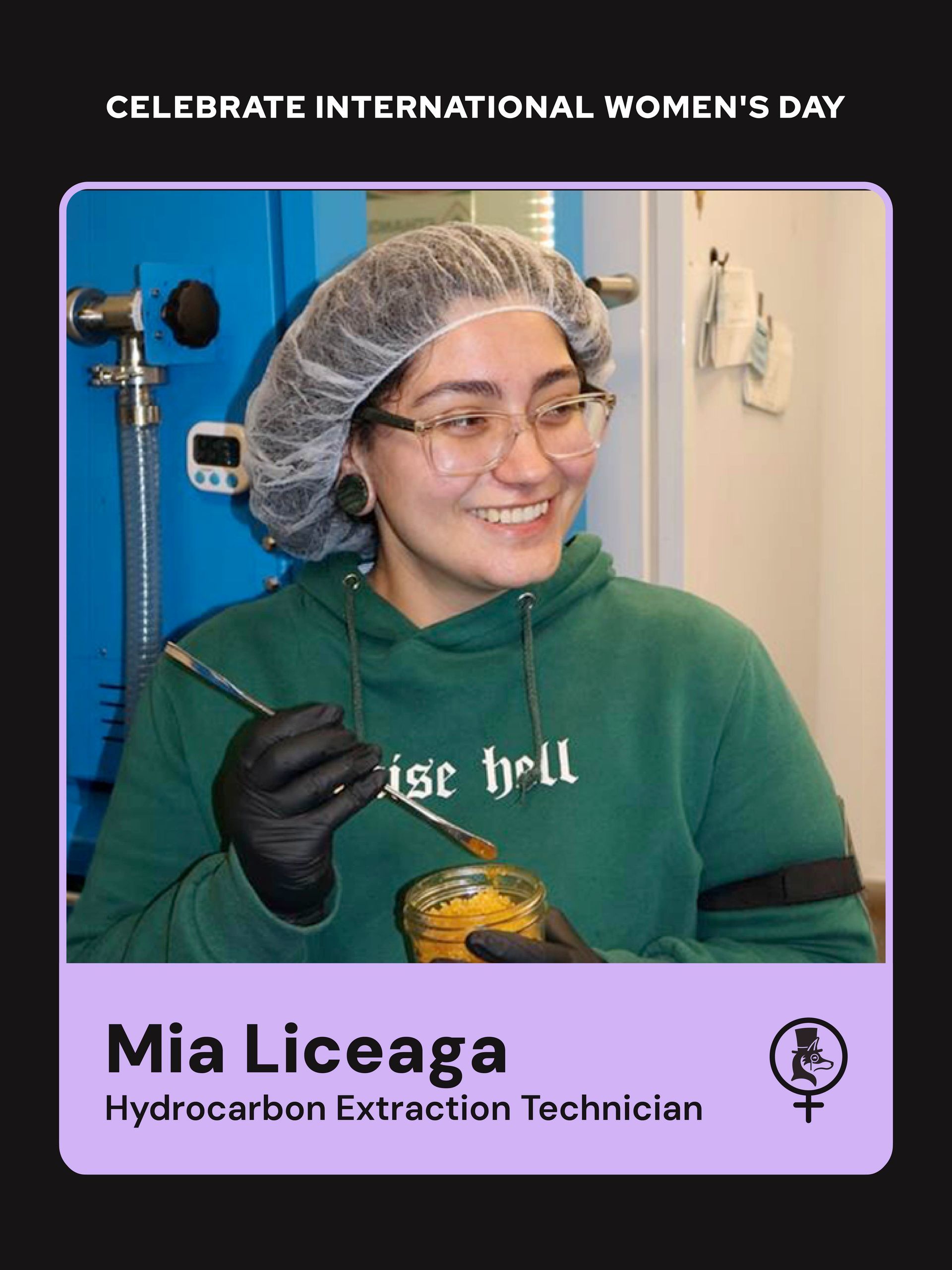 Hydrocarbon extraction technician smiling in hairnet and gloves, holding a tool beside a blue machine.