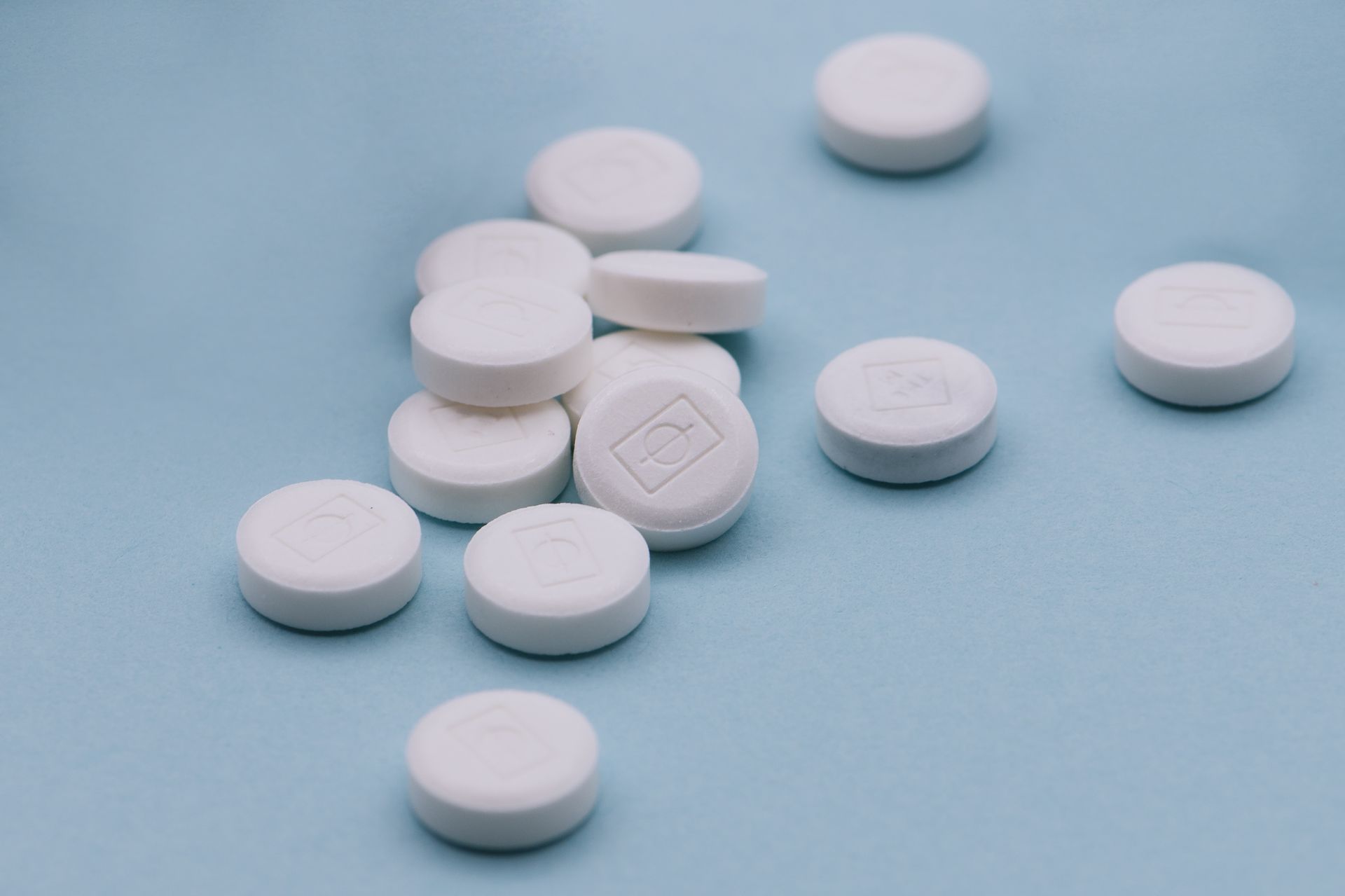 White round tablets scattered on a light blue surface, with one embossed tablet in the center