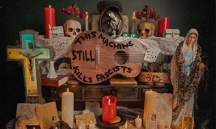 Memorial altar with candles, flowers, and signs reading “This machine still kills fascists” and a cross