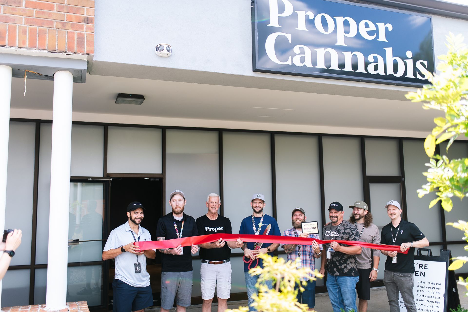 Ribbon-cutting outside Proper Cannabis storefront with five people posing behind a red ribbon