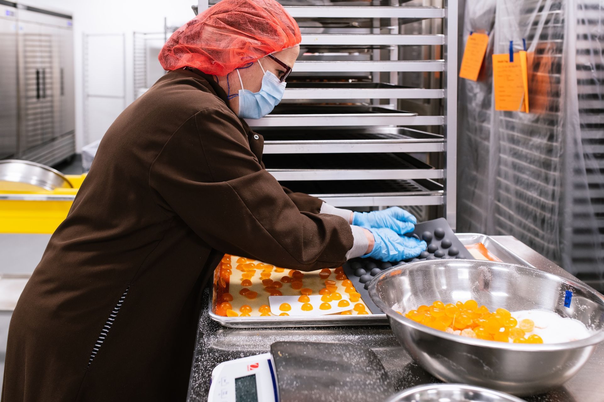 Worker in hairnet and mask arranging pastries on trays in a commercial kitchen