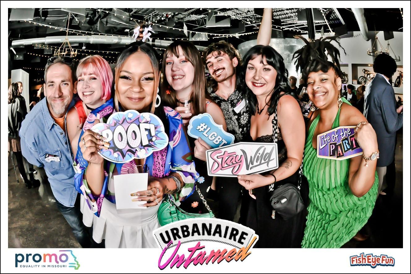 Six smiling people holding colorful signs at Urbanaire event backdrop