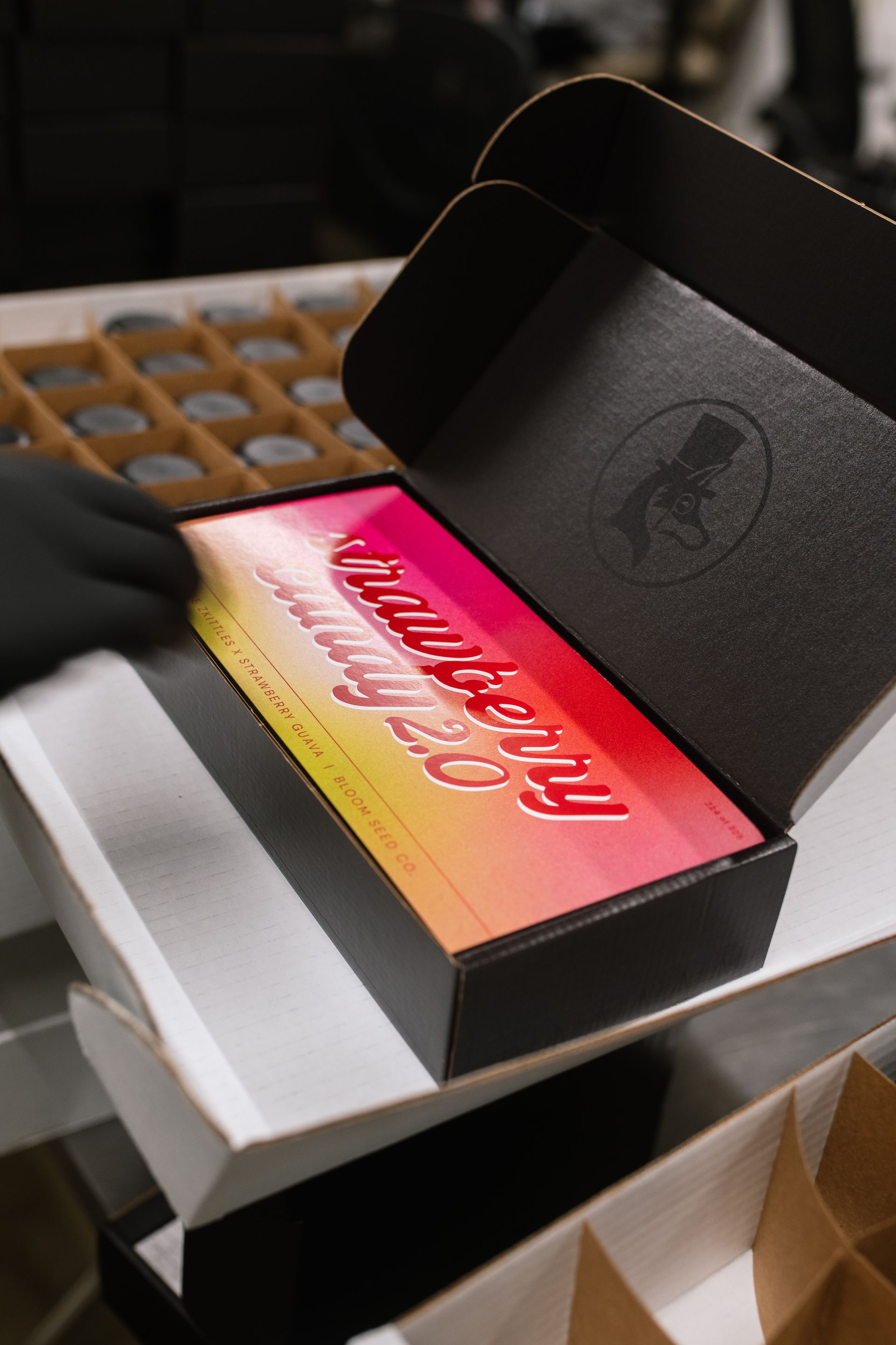 Black box with a pink-and-orange card insert on a table, with a gloved hand nearby.