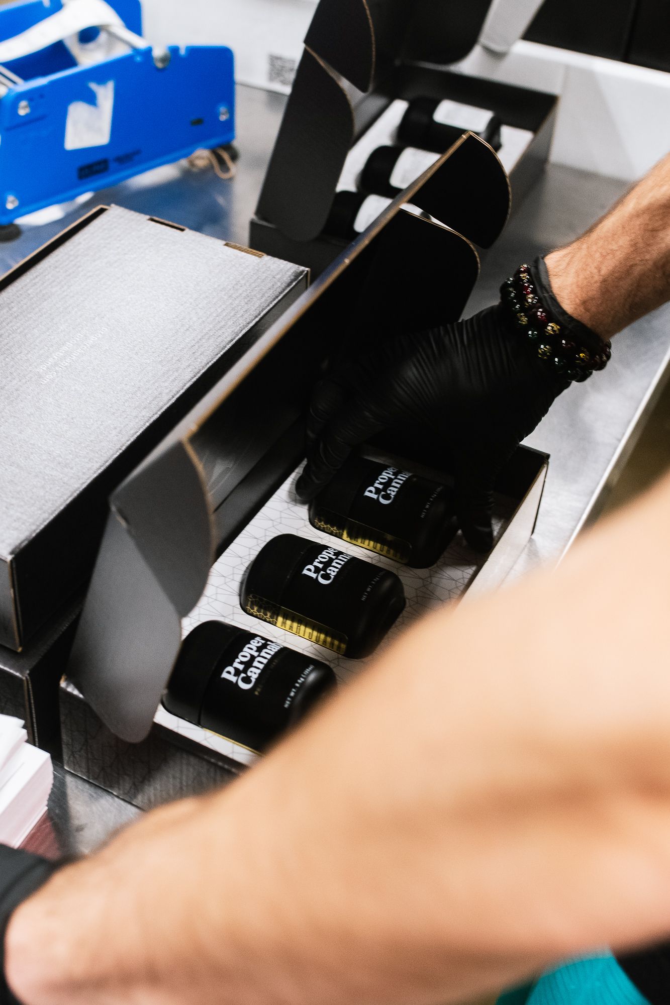 Gloved hands packing black bottles into a box on an assembly line