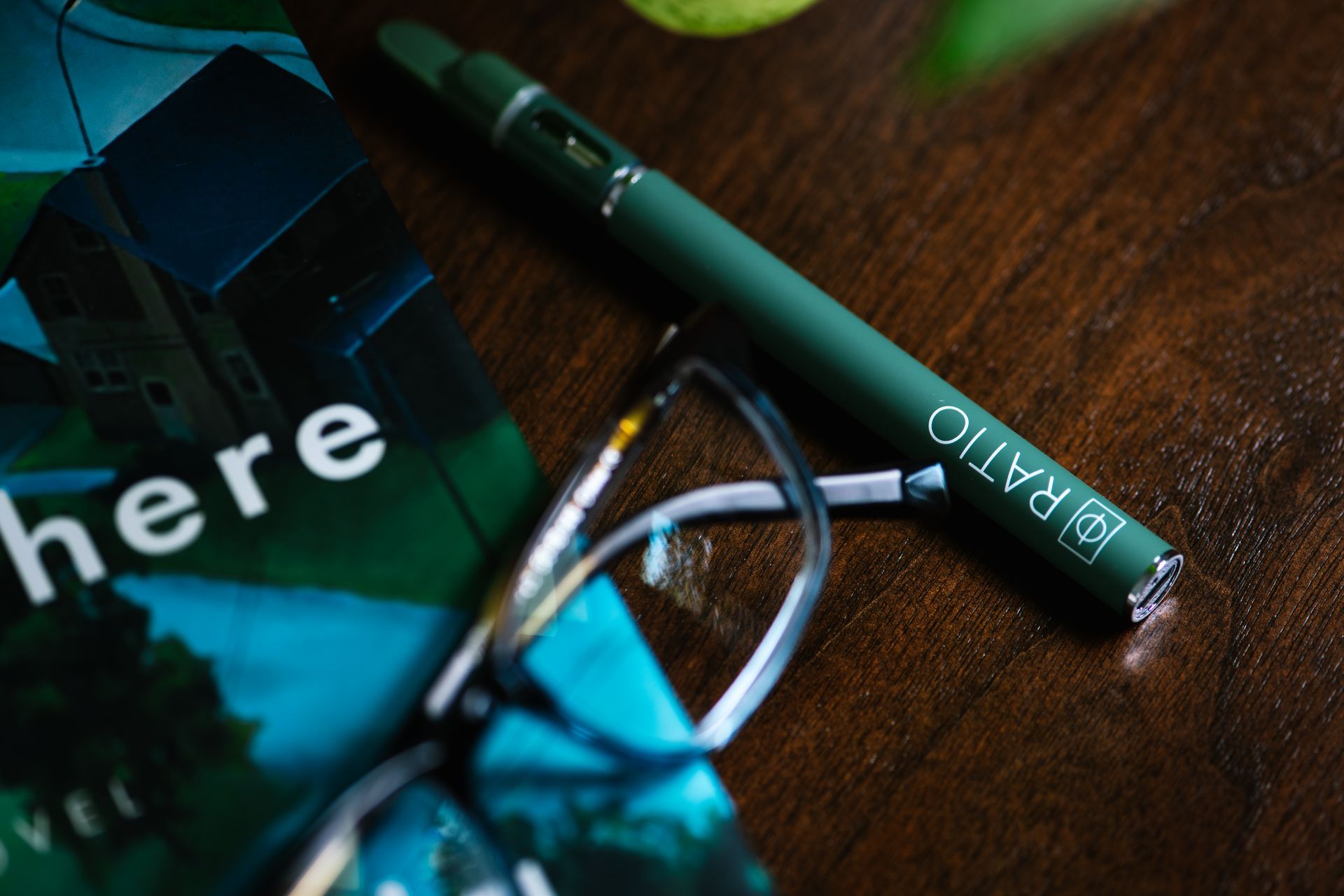 Green pen and eyeglasses on a wooden table beside a teal card with the word “here”