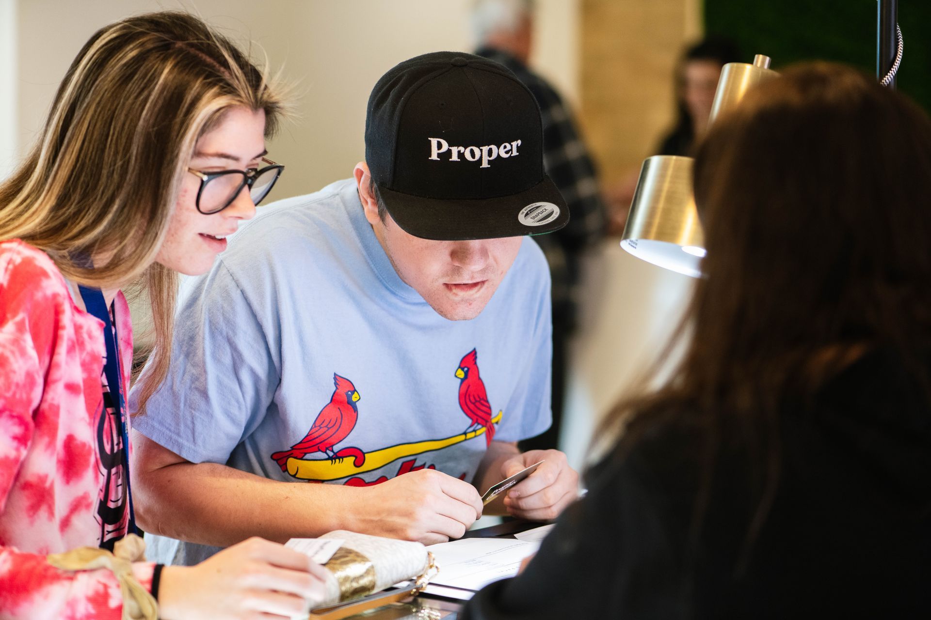 Three people collaborating at a table, writing on papers under a desk lamp