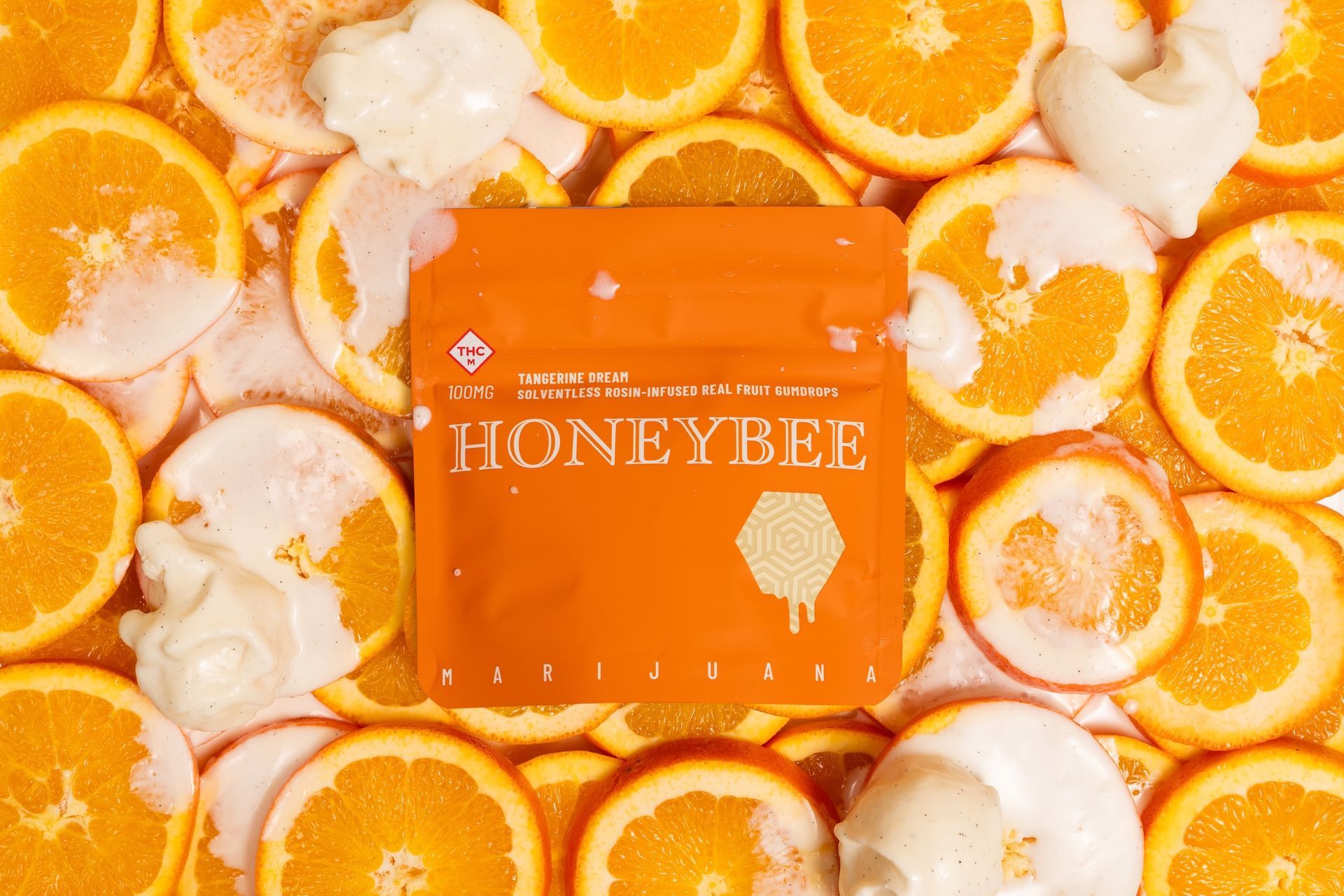 Orange honeybee product box surrounded by orange slices and white flower petals