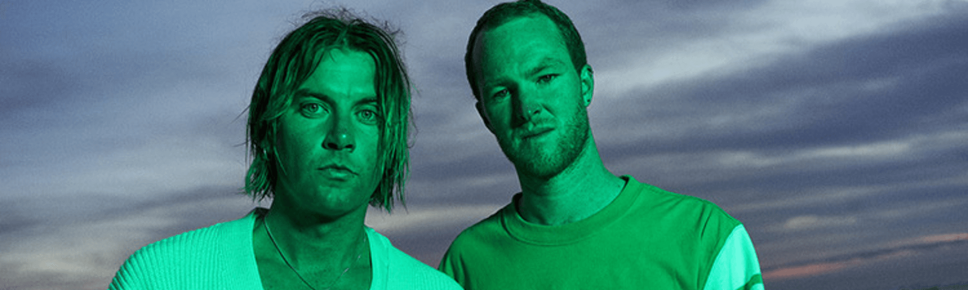 Two people standing outdoors at dusk with a green color cast, facing the camera.