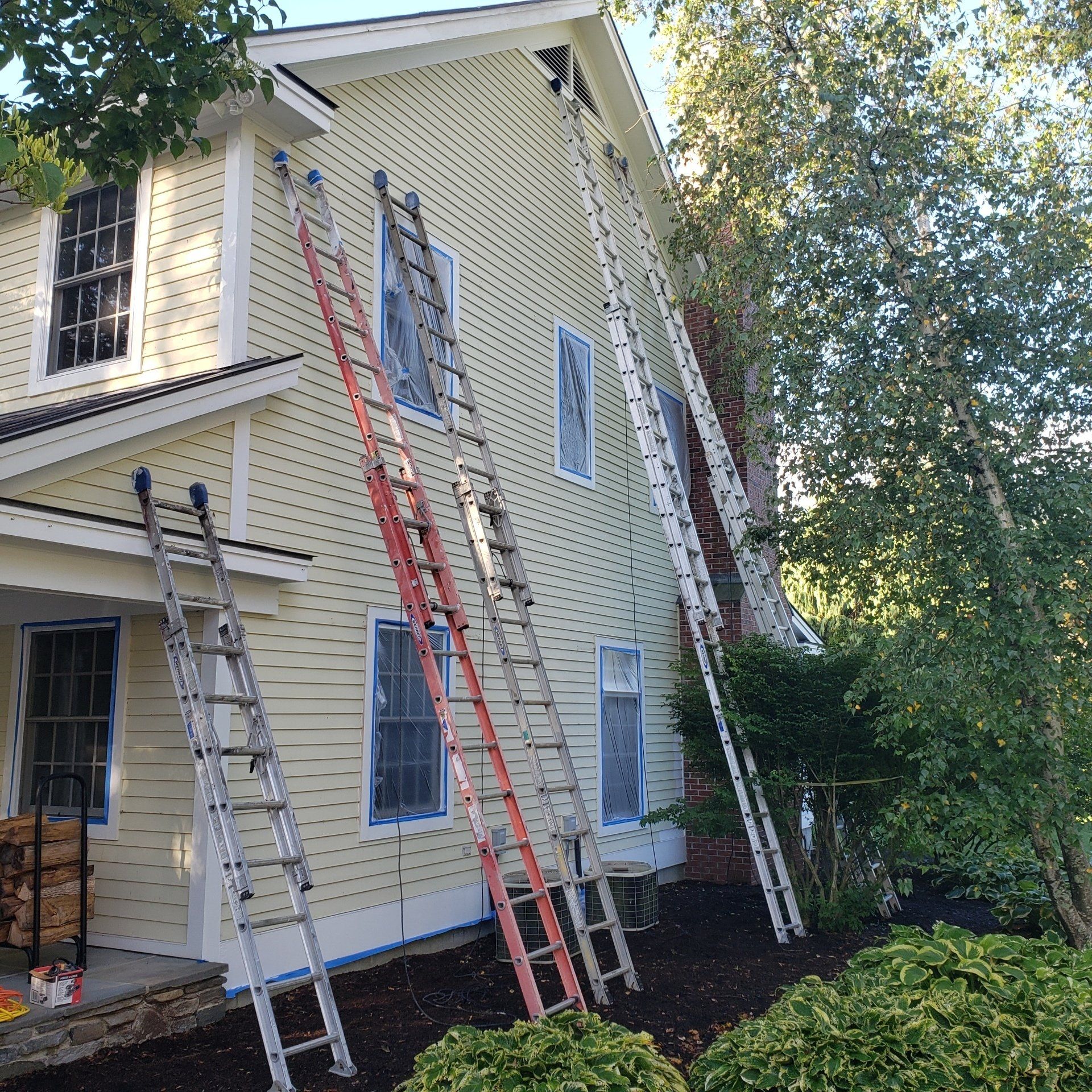 A house is being painted with ladders on the side of it.