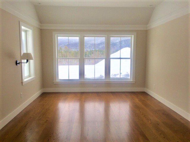 An empty room with hardwood floors and three windows.