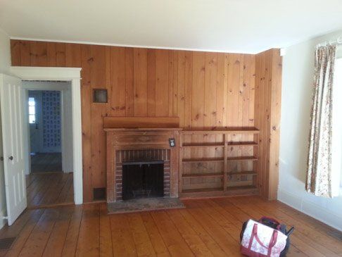 An empty living room with wood paneling and a fireplace