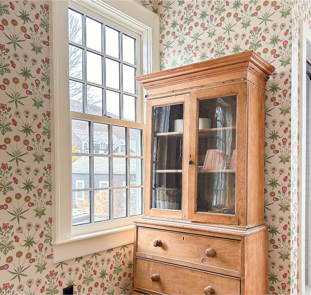 A wooden cabinet with glass doors sits in front of a window