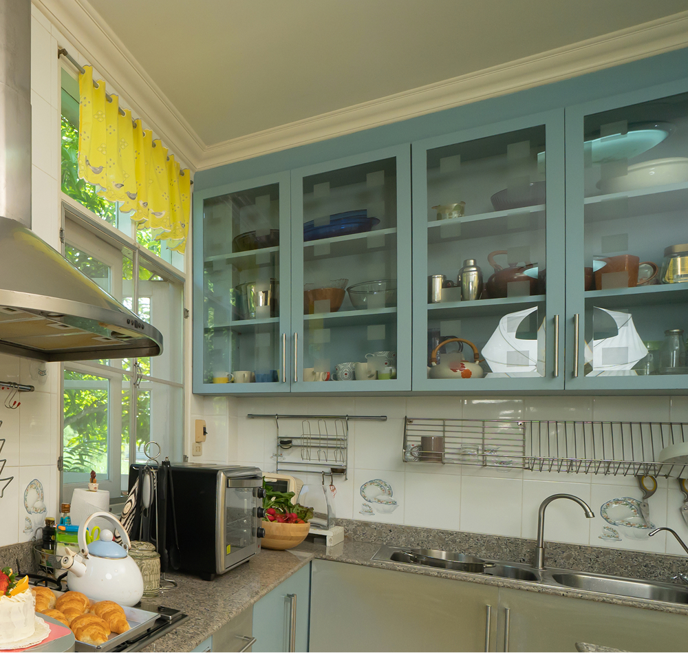 Kitchen with blue cabinets, glass doors, and a window with yellow curtains.