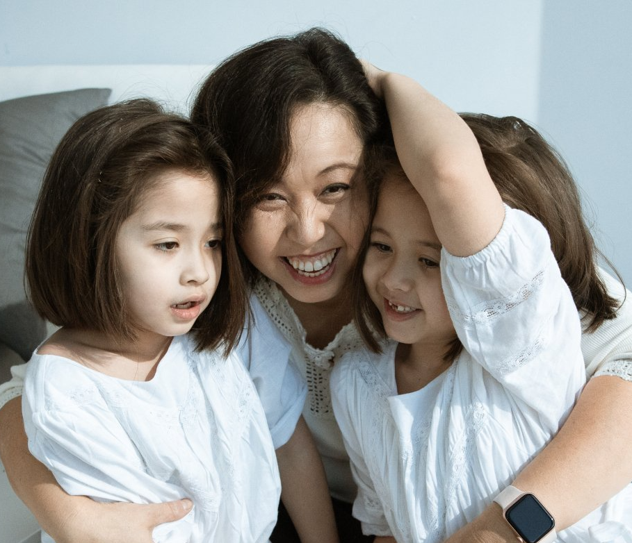 A woman is hugging two little girls on a bed.