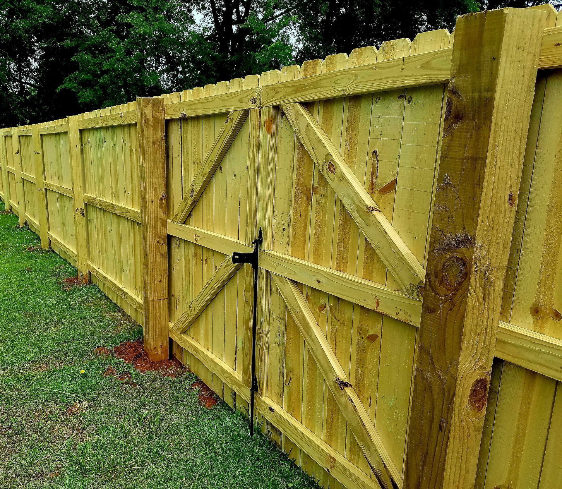 Wooden fence with gate in a yard. Green grass and trees in background.