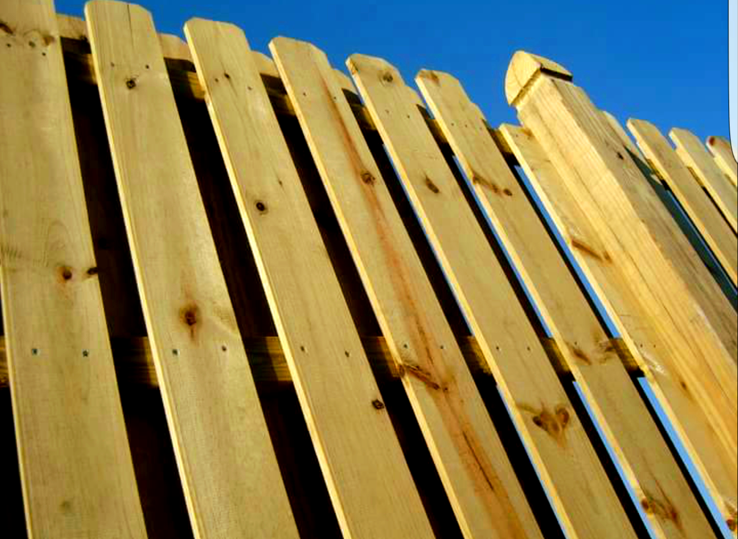 Wooden fence against a bright blue sky, angled perspective, light brown wood.