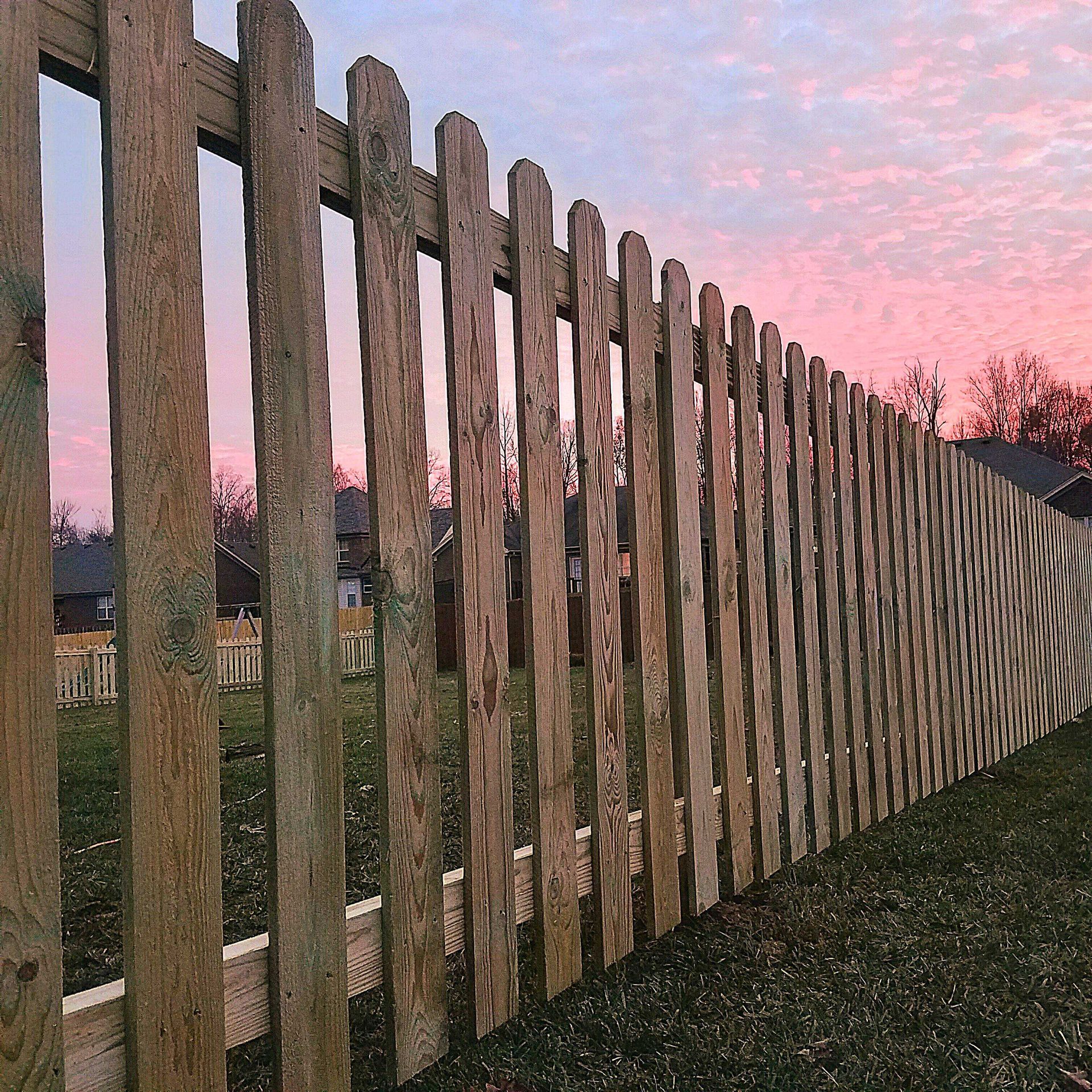 Wooden picket fence with a colorful pink and orange sunset in the background.