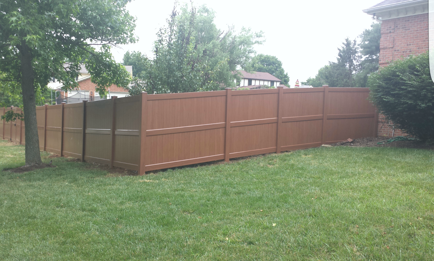 Brown privacy fence in a grassy yard, next to a brick house and trees.