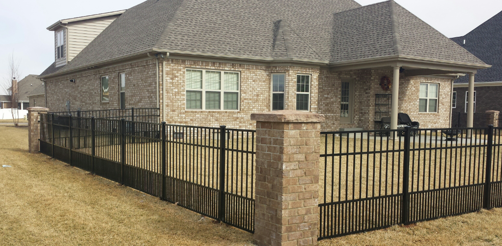 Brick house behind a black metal fence, on dry brown grass.