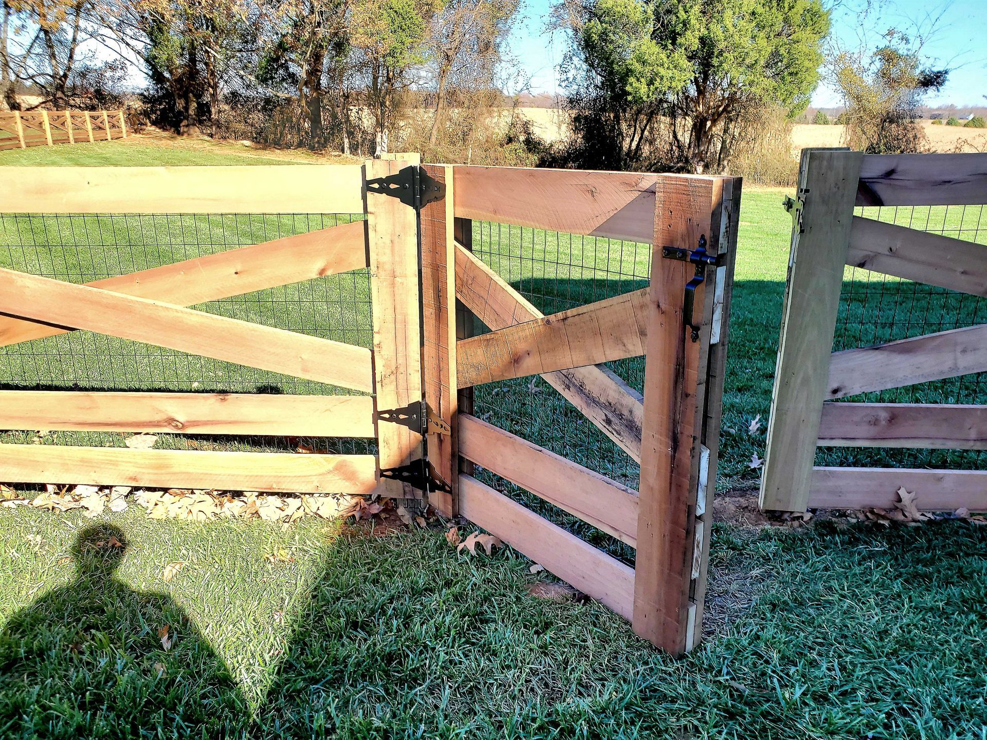 Wooden gate in an open position in a grassy yard, part of a wooden fence.
