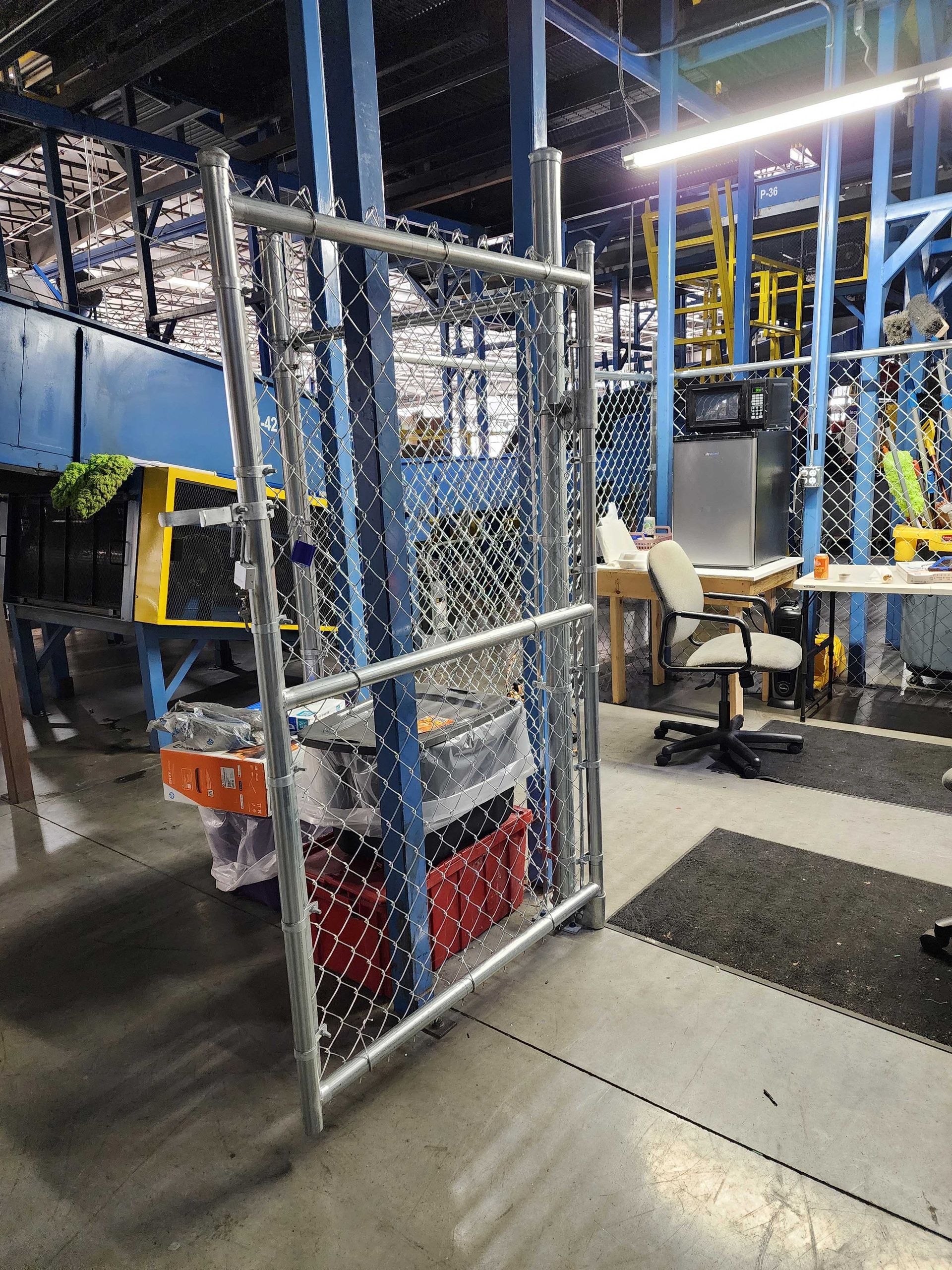 Chain-link gate in a warehouse setting, partially blocking view of bins and office area.