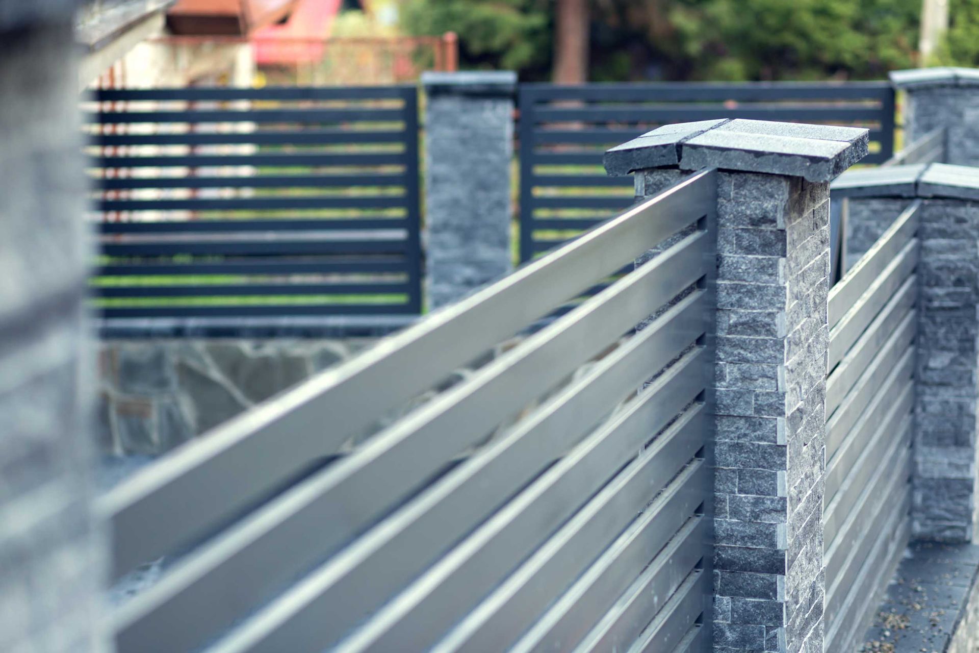 Modern metal fence with stone pillars along a residential property. Modern metal fence with stone pillars along a residential property.