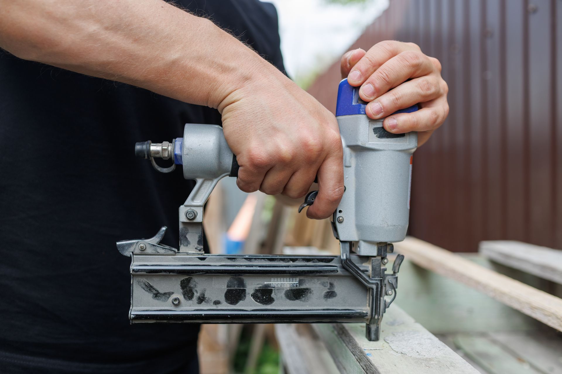 Carpenter using pneumatic nail gun on wood during outdoor fence or deck installation.