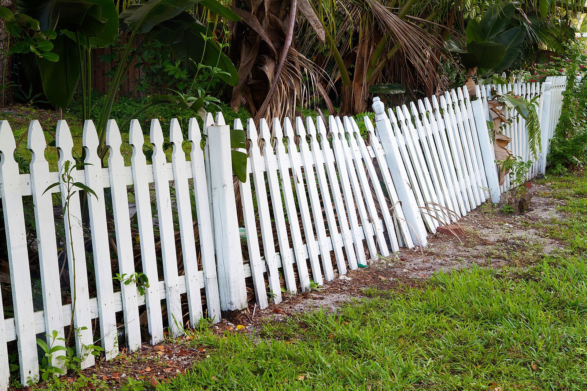 Leaning white picket fence needing fence repair in a residential yard