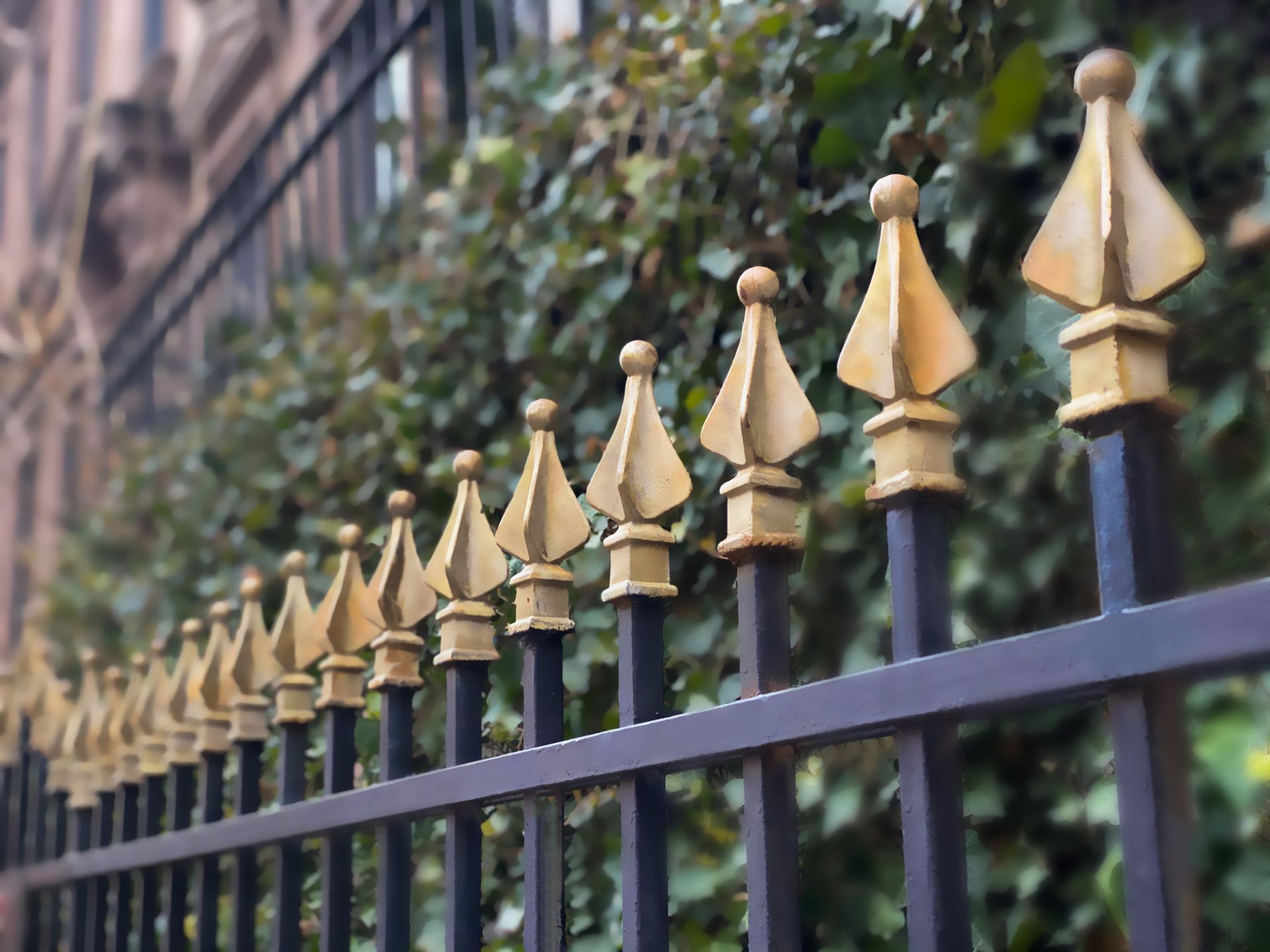 A close up of a wrought iron fence with gold spikes in front of a building.