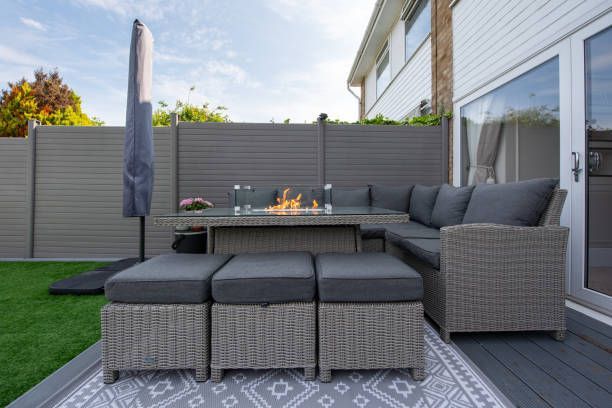 A patio with a couch , table , ottomans and a fire pit.