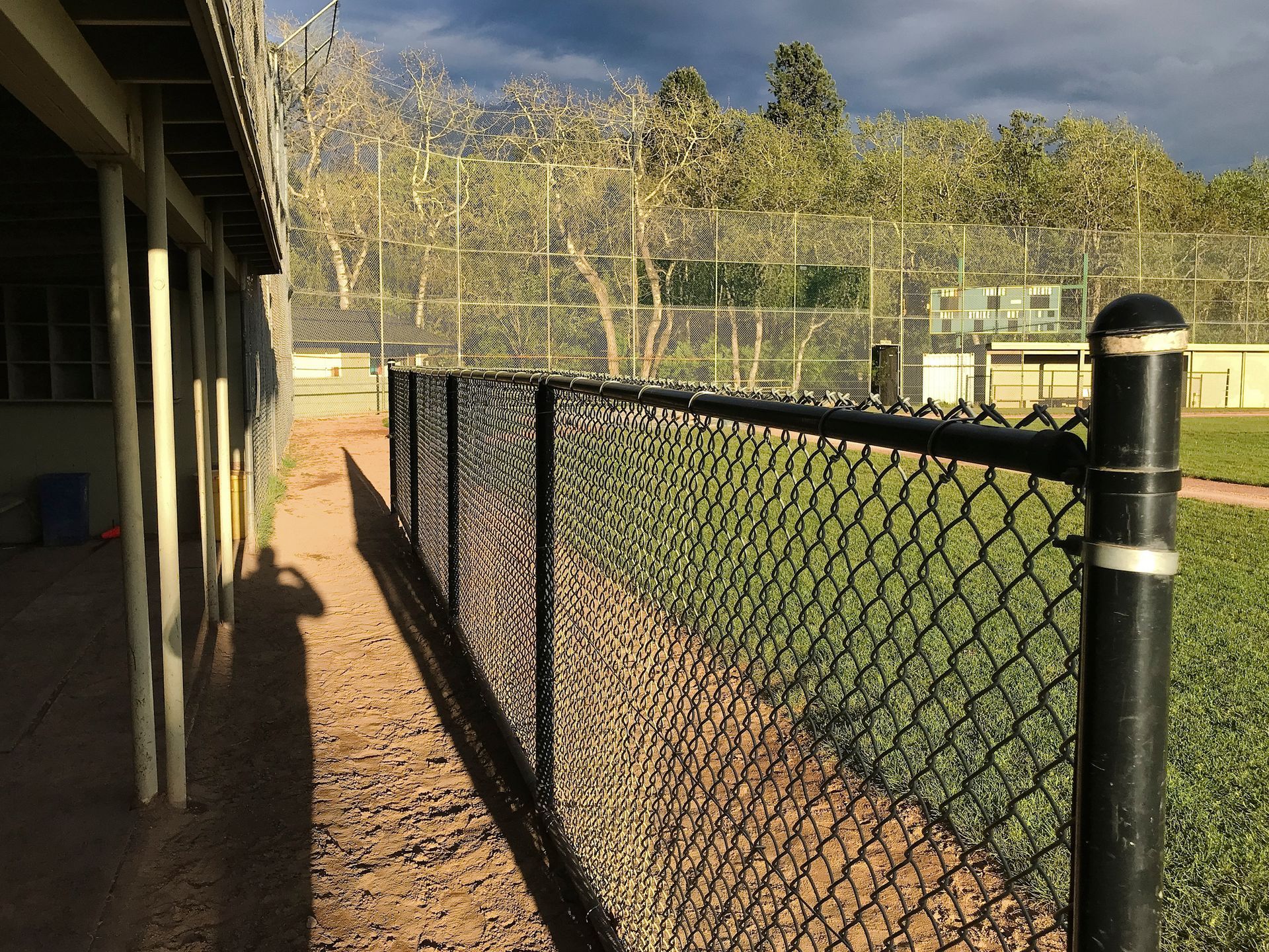 Black chain-link fence along a baseball field, next to a covered dugout.