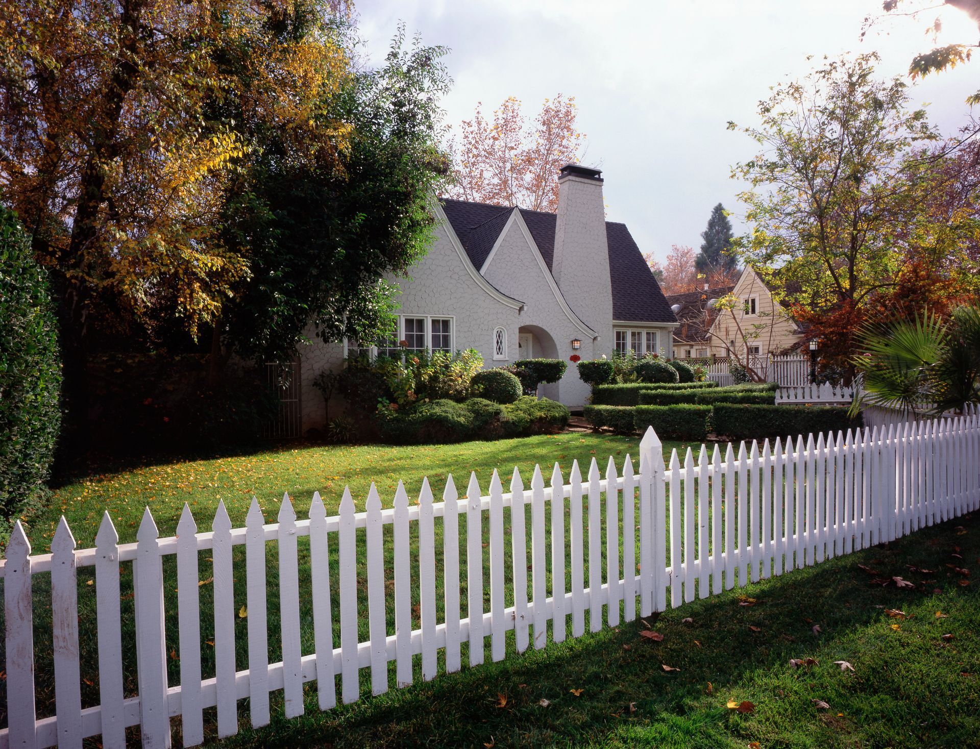 A white wooden fence with a hedge in the background.