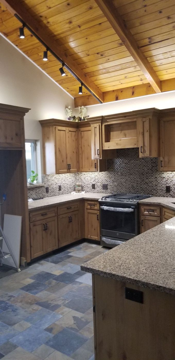 A kitchen with wooden cabinets , granite counter tops , a stove and a wooden ceiling.