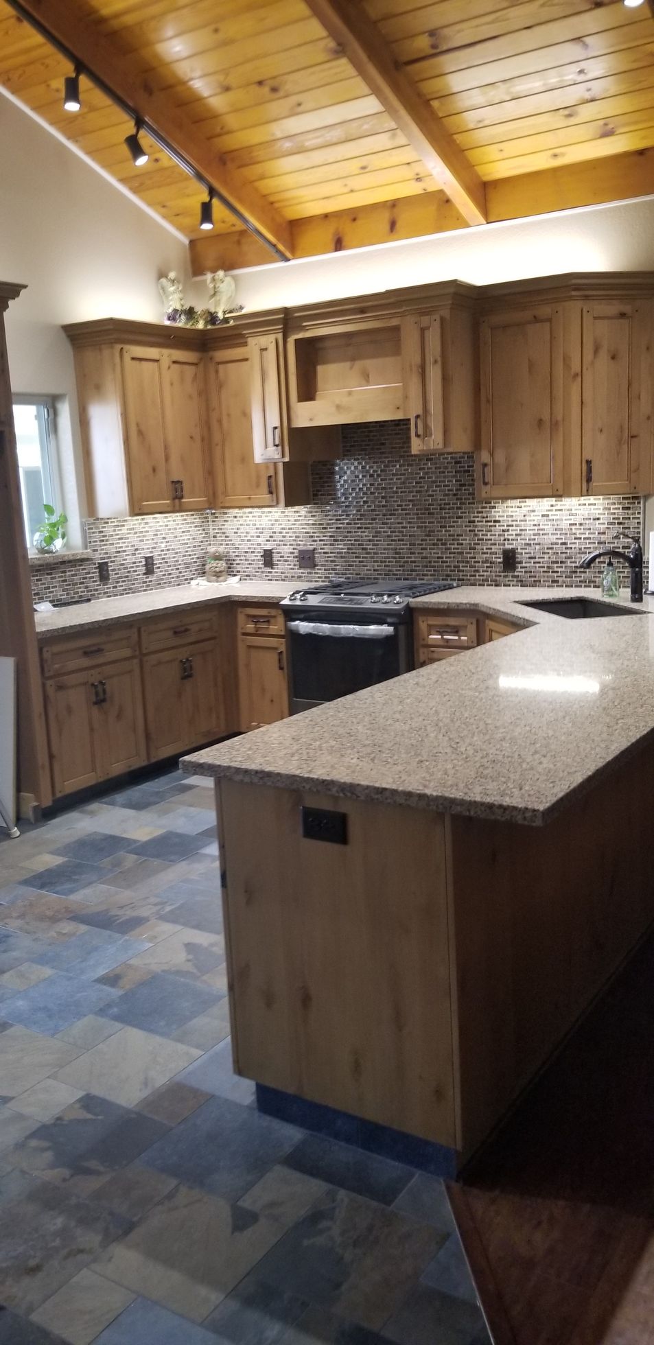 A kitchen with wooden cabinets , granite counter tops , a stove , and a large island.