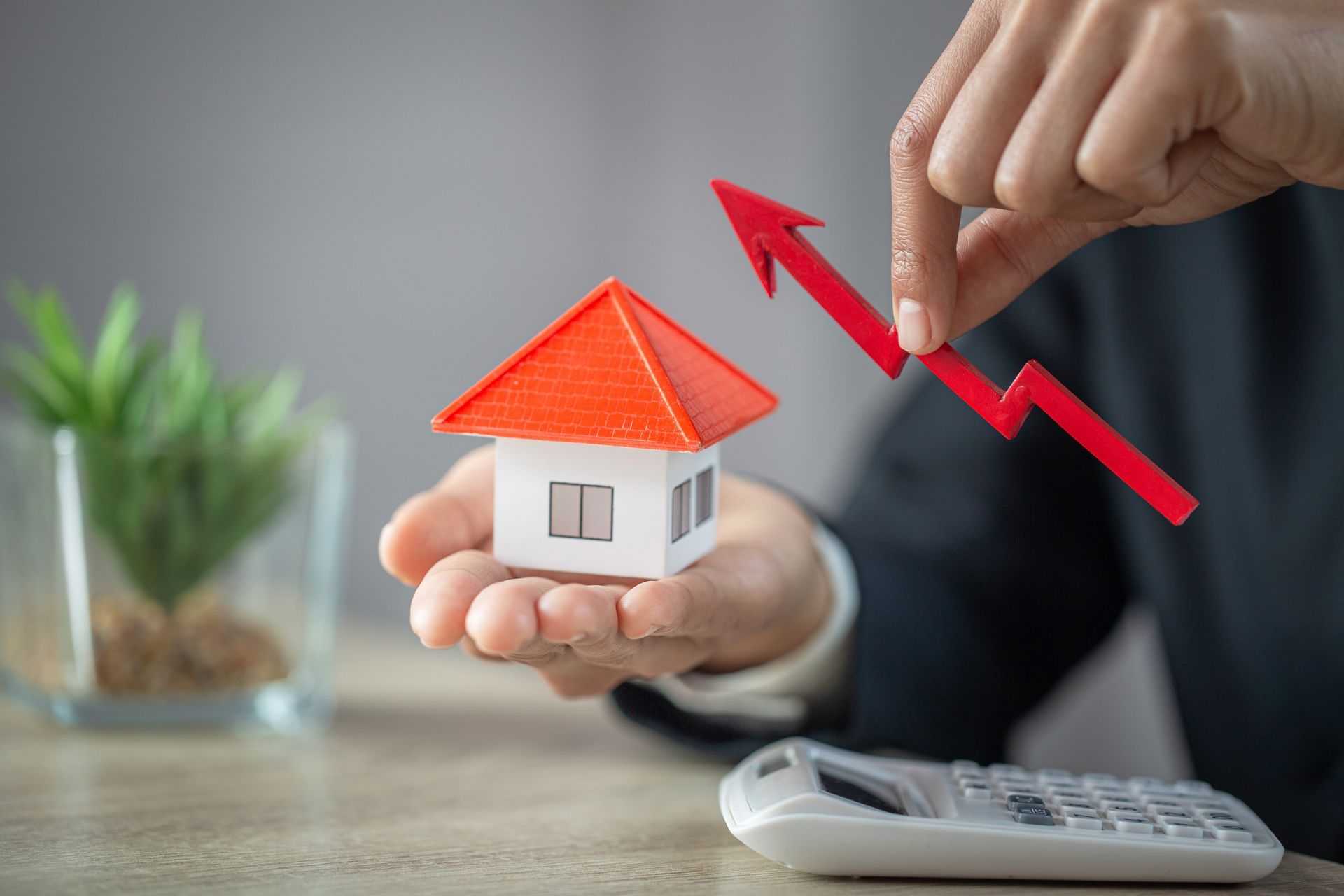 A person is holding a model house with an arrow pointing up.