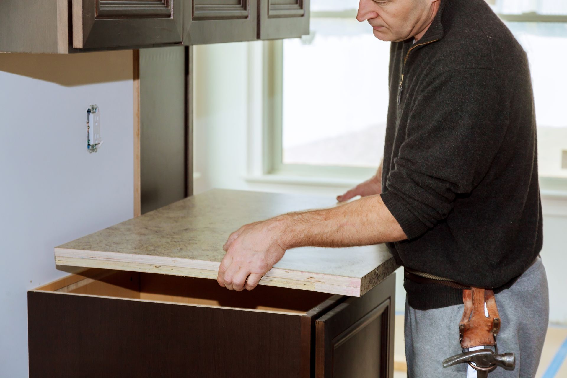 A man is holding a hammer while working on a kitchen counter