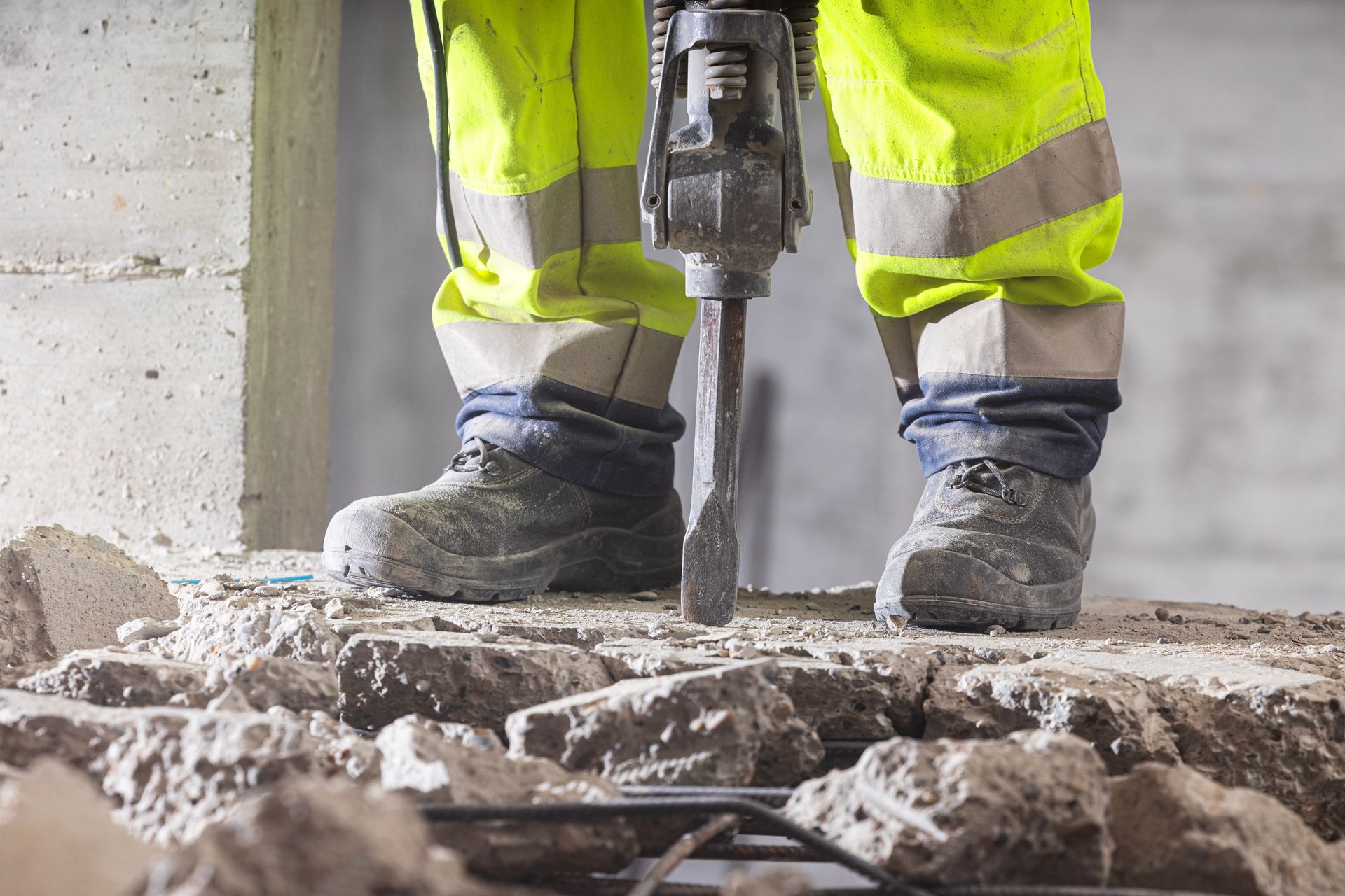 A construction worker is using a hammer to break concrete.