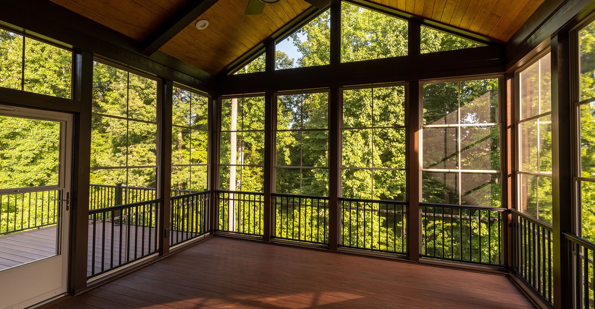 A screened in porch with lots of windows and trees in the background.