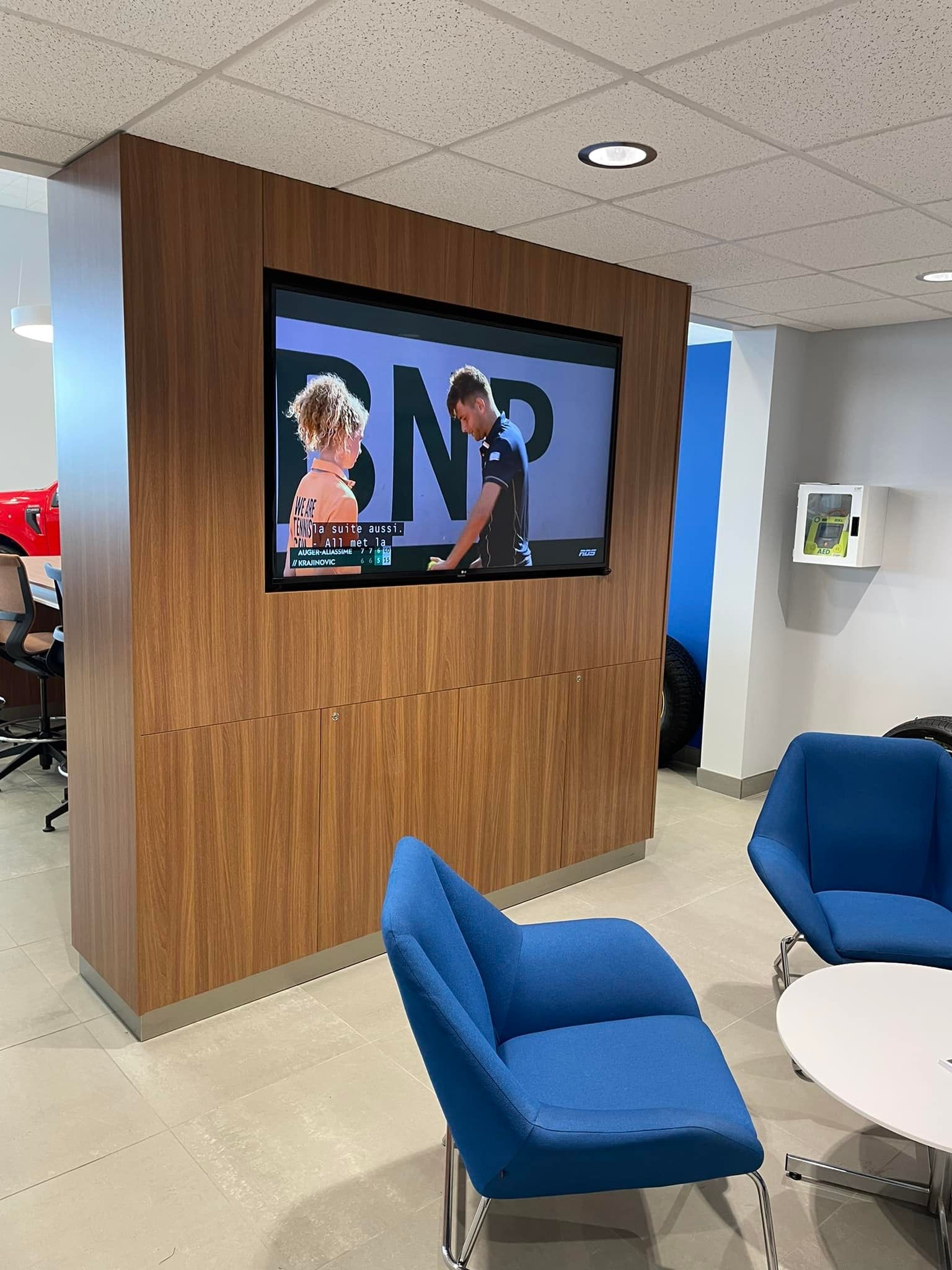 A room with blue chairs and a tv on the wall that says bnp