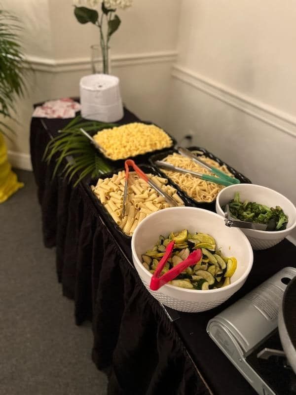Buffet table with assorted salads and dishes in white bowls and trays, set against a cream wall.