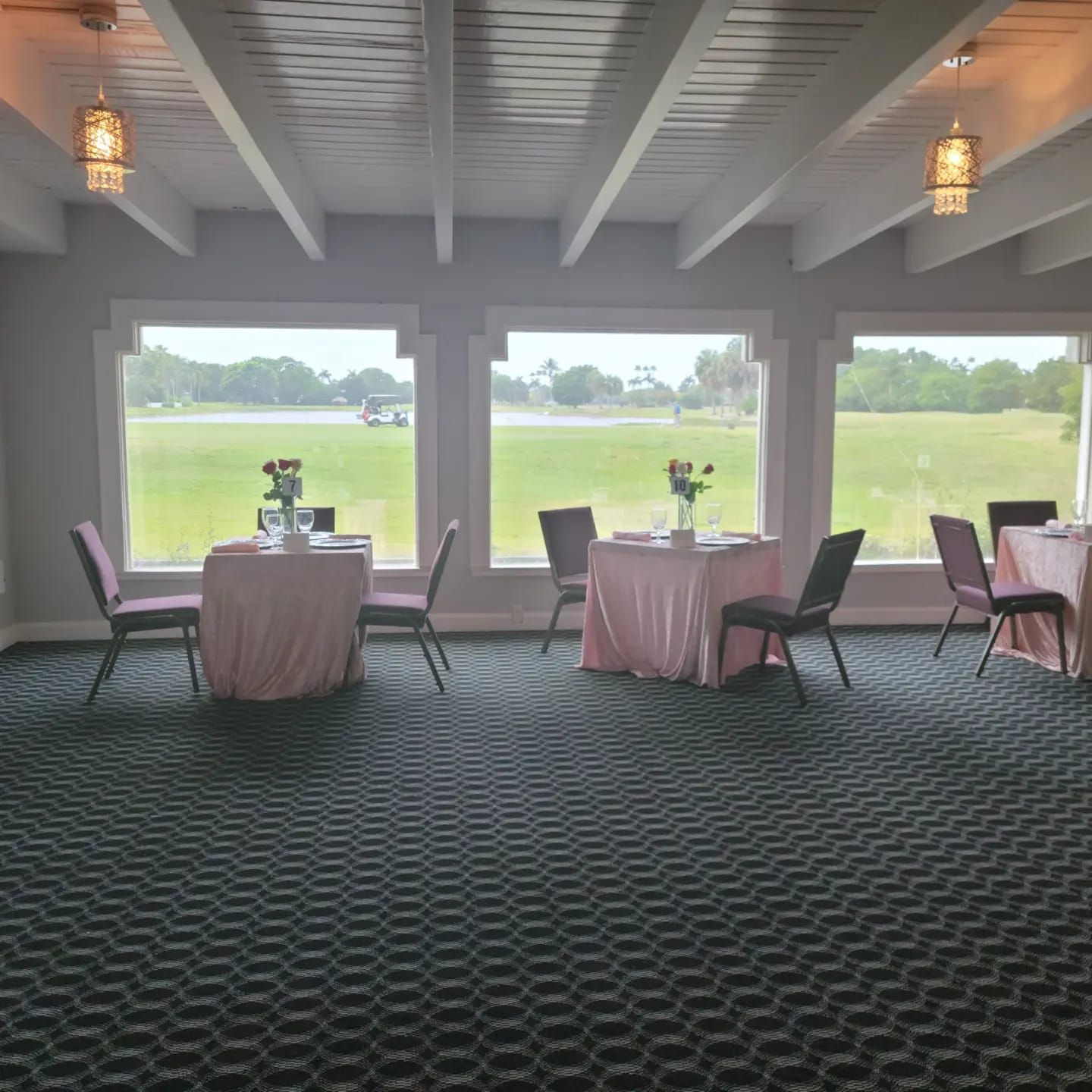 Empty banquet room with round tables, chairs, and large windows overlooking a green field