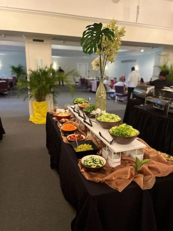 Buffet table with assorted dishes and a tall floral centerpiece in a conference room