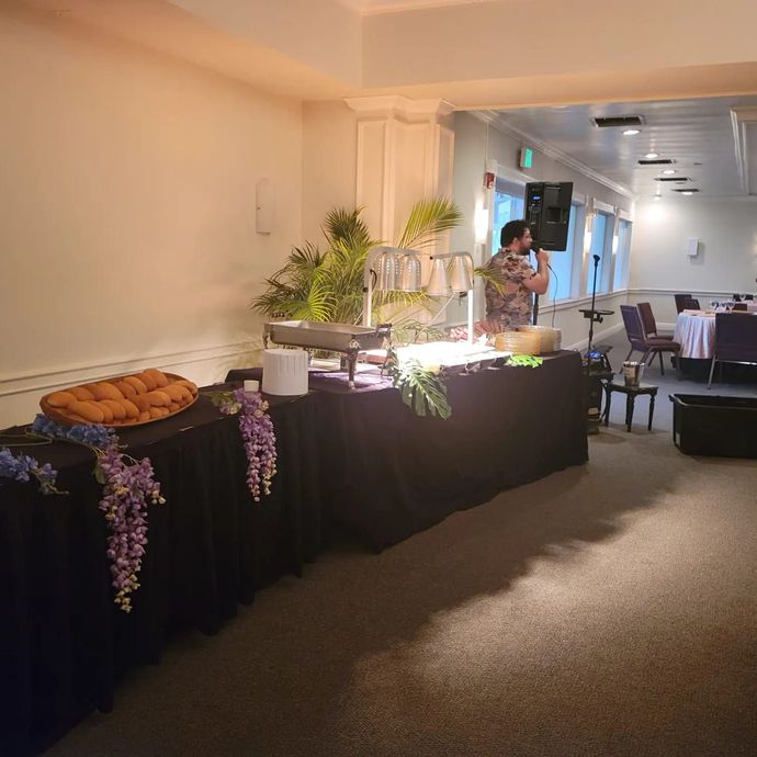 Buffet table with pastries and greenery in a bright hallway, with guests seated in the background