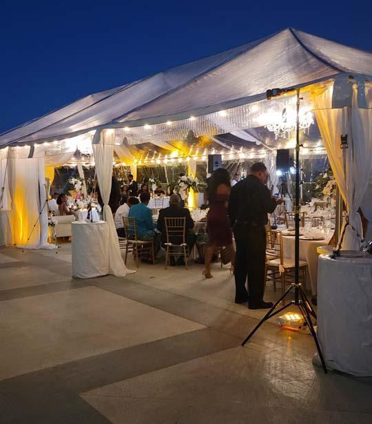 Outdoor evening tented reception with guests, tables, and warm string lights at a formal event