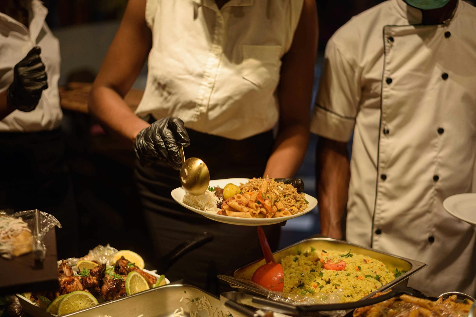 Chefs serving buffet dishes, including pasta and a yellow casserole, at a restaurant counter