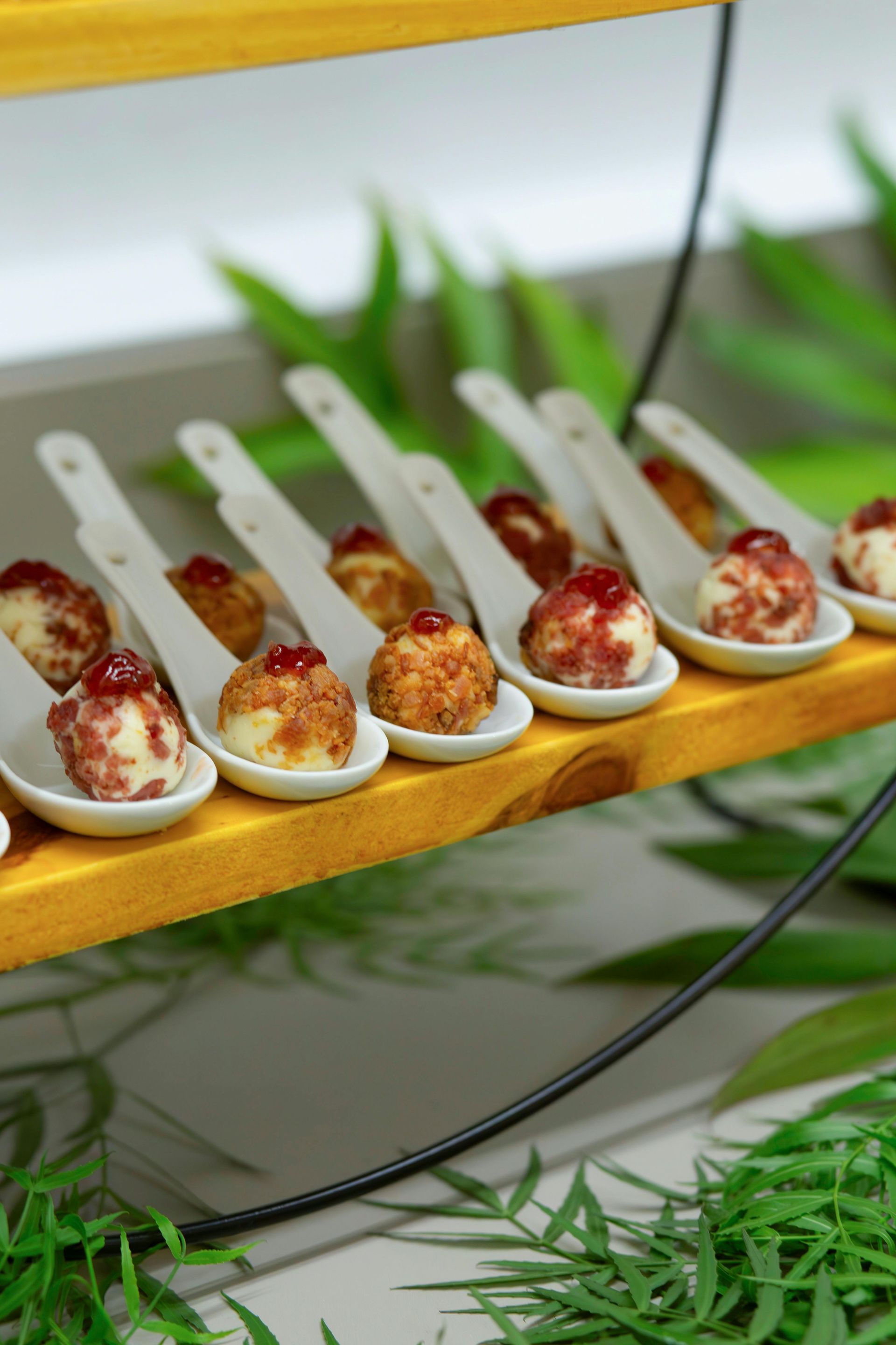 White spoons of bite-sized appetizers on a wooden stand, garnished and arranged in a row.