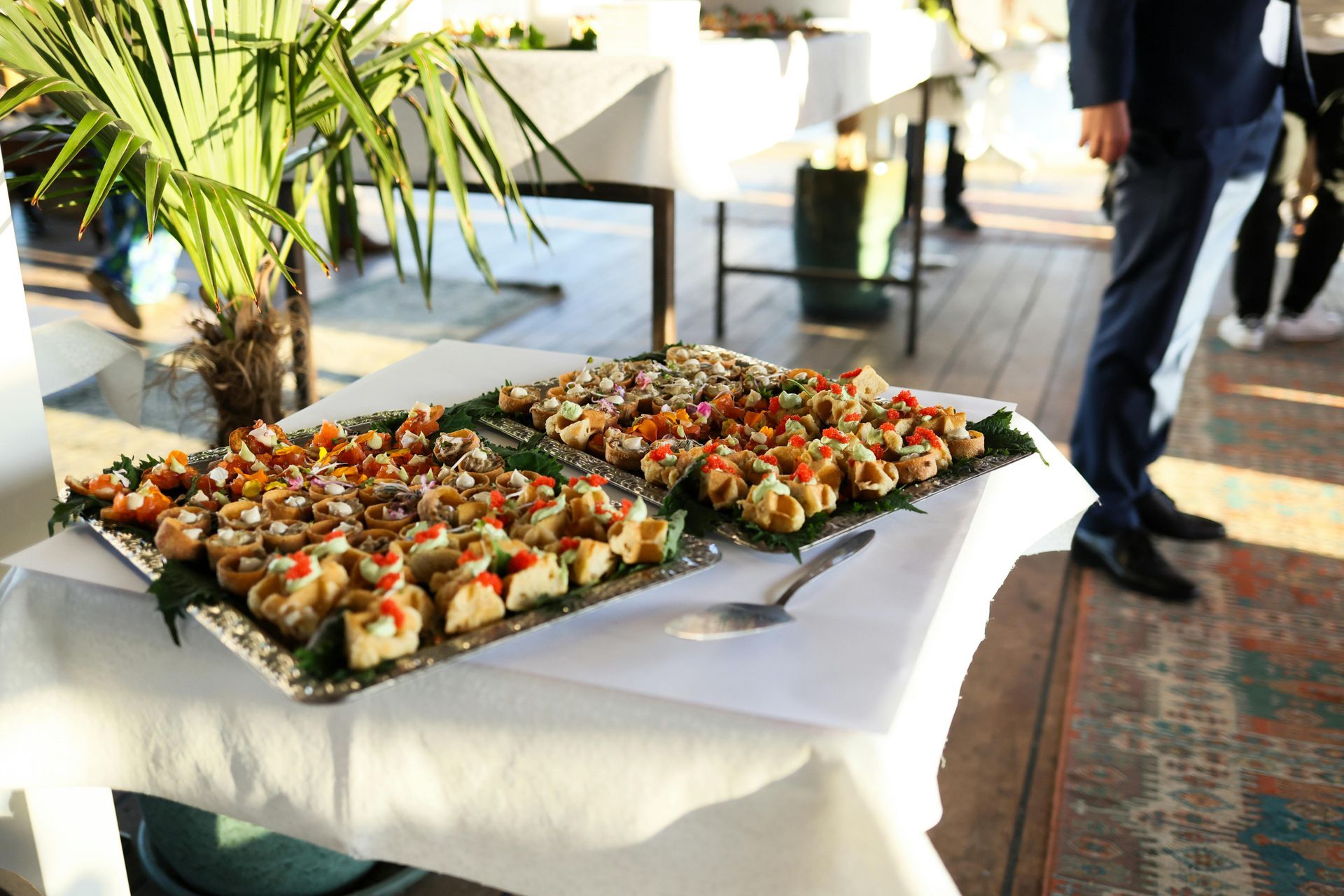 Tray of bite-sized hors d'oeuvres on a table at an indoor event, with people walking nearby